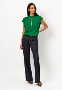 Groen T-shirt met korte mouwen en een ontspannen pasvorm, gecombineerd met donkerblauwe wijde jeans. Gevoerde flats met luipaardprint en gelaagde zilveren kettingen.