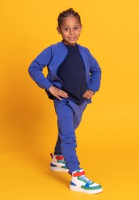 Niebieski dres z kurtką na zamek i dopasowanymi spodniami, zestawiony z białymi trampkami z kolorowymi akcentami i wzorami na cholewce.