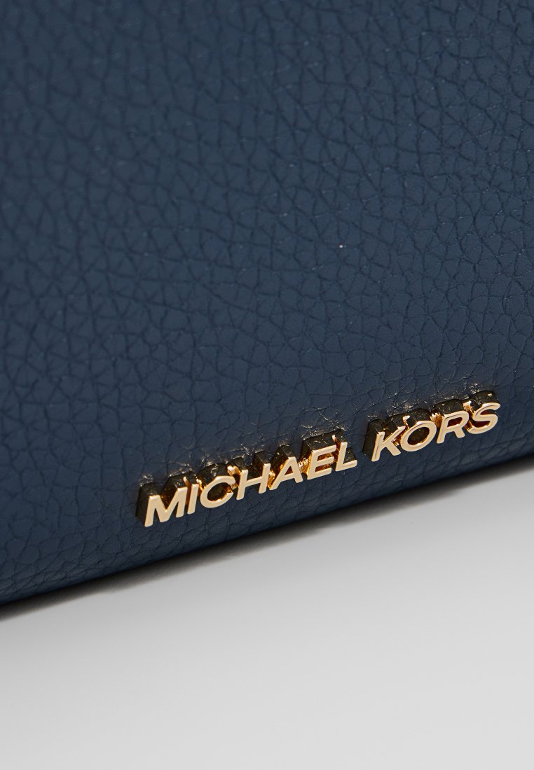 Sac à main en cuir texturé bleu avec le logo doré "MICHAEL KORS". La surface présente un motif fin et granuleux ainsi qu'une forme structurée.