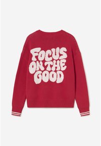 Pull en maille rouge avec un grand texte blanc "Focus on the Good" au dos et des poignets rayés blancs sur les manches.