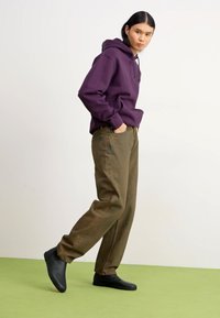 Sudadera de algodón púrpura sobre pantalones de pierna ancha verde olivo; modelo con zapatos negros; ligera textura visible en la tela; fondo liso.