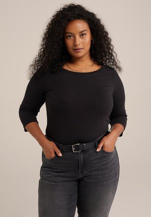 Black long-sleeve top made from stretchy fabric, featuring a scoop neckline and a fitted design. Paired with dark jeans and a black belt.