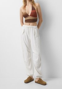 Top de cuello halter en tonos marrón degradado con un diseño ajustado, combinado con pantalones de lino blanco de corte amplio y zuecos marrones.