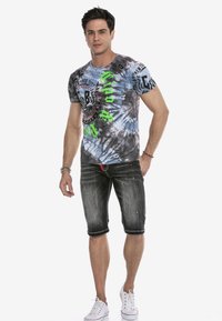 Kurzärmeliges Batik-T-Shirt in Blau und Grau mit grünem grafischen Druck, kombiniert mit ausgefransten schwarzen Jeansshorts und weißen Sneakern.