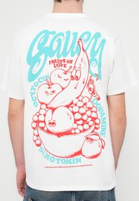 Bílé bavlněné tričko s barevným grafickým potiskem na zádech, zobrazujícím karikatury ovoce a stylizovaný text v červené a modré barvě.