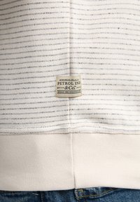 Suéter de color claro con rayas horizontales azul marino, tejido texturizado y puño acanalado. Cuenta con una etiqueta rectangular de la marca en el bajo.