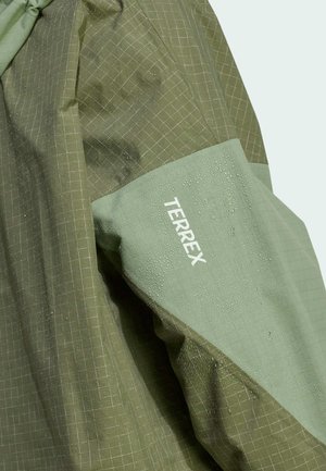 Green waterproof jacket featuring a textured grid pattern, with a smooth lighter green sleeve section displaying "TERREX" logo and water droplets.