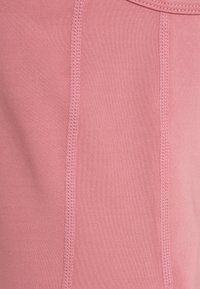 Rosa stretchtyg med synliga sömmar och en slät textur. Designen har en enkel, figursydd form utan ytterligare detaljer.