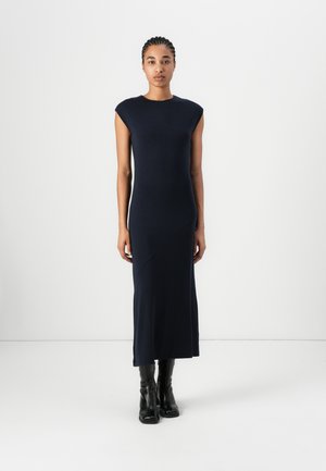 Marineblaue, eng anliegende Midikleid mit kurzen Ärmeln, glatter Textur und asymmetrischem Nähdetail. Kombiniert mit kniehohen schwarzen Stiefeln.