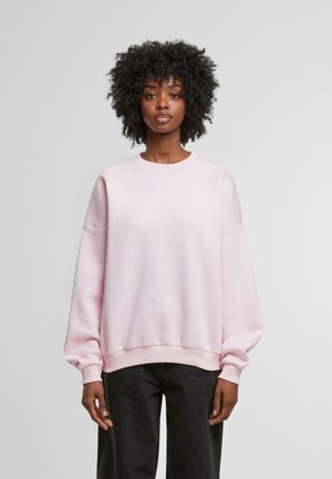 Svetlo roza sweatshirt iz mehkega materiala, s krožnim izrezom in povečanimi, obsežnimi rokavi. Diskretna vezenina logotipa spredaj.