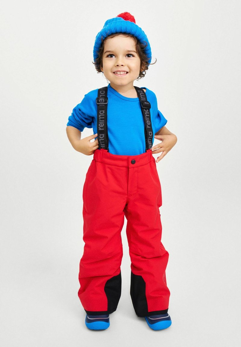 Röda vattentäta snöbyxor med svarta detaljer, justerbara hängslen och en blå långärmad tröja; blå stickad mössa med röd pom-pom.