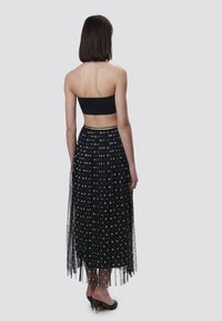 Bandeau noir associé à une jupe maxi transparente noire à pois blancs, avec une ceinture rehaussée d'or. Chaussures à talons hauts noires.