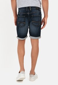Denimshorts, mørkeblå med opsmøg, prydet med to baglommer med kontrasterende syninger og et mærke på livbåndet.