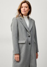 Grijze wollen jas met een op maat gemaakt ontwerp, met revers, twee voorkruiden zakken en twee zwarte knopen, met een gladde textuur en een gemiddelde lengte.