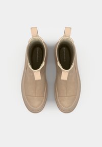 Botines de ante beige con paneles laterales elásticos y tiradores, acabado suave y suelas de goma, con un diseño simple y limpio.