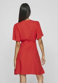 Abito rosso con maniche corte, cuciture delle spalle arricciate, vita stretta e gonna svasata, realizzato in un tessuto leggero con una consistenza morbida.