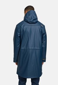 Lange, marineblauwe waterdichte jas met een capuchon, met een gladde textuur, zichtbare naden en een subtiel logo op de schouder.