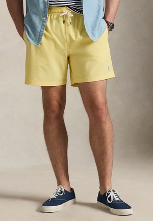 Kollased ujumispüksid, millel on elastne vöökoht ja valge nöör. Sobitatud helesinise nööpidega särgi ja tumesiniste tossudega.