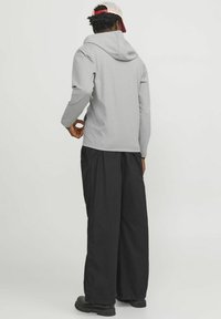 Sudadera gris con capucha y mangas largas, combinada con pantalones negros holgados y botas negras resistentes. Un atuendo visualmente sencillo y casual.