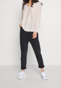 Kremowy sweter z dekoltem w serek i długimi rękawami, zestawiony z podwiniętymi ciemnymi spodniami i białymi trampkami. Miękka faktura i luźny krój.