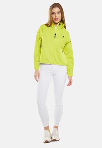 Limegrön fleecejacka med hög krage och dragkedja. Har sidofickor och en liten logo på vänster bröst. Slät yta.