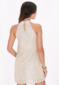 Rochie halter din mătase ușoară bej, cu paiete argintii. Prezintă un decolteu în formă de cheiță la spate și un design lejer, fluid. Textură netedă.