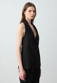 Gilet in lino nero con scollatura a V profonda, chiusura a un solo bottone e tasche laterali. Presenta una vestibilità sartoriale e linee pulite e semplici.