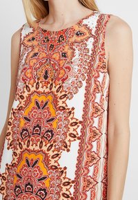 Ärmelloses Kleid mit aufwendigen orange-rot Paisleymustern auf weißem Grund, mit einem runden Ausschnitt und dezenten Perlenakzenten.