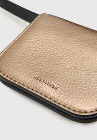 Tarjetero de piel texturizada en color dorado con bordes negros. Presenta el logo embellecido "ALLSAINTS" en el lateral, destacando una forma rectangular elegante.