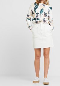 Top de manga larga con estampado floral de hojas verdes y rosas, combinado con una falda de mezclilla blanca que tiene bolsillos frontales y un dobladillo por encima de la rodilla.