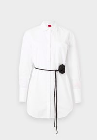 White button-up shirt with long sleeves, chest pocket, and a black fabric belt featuring a rosette detail. Cotton material with a smooth texture.