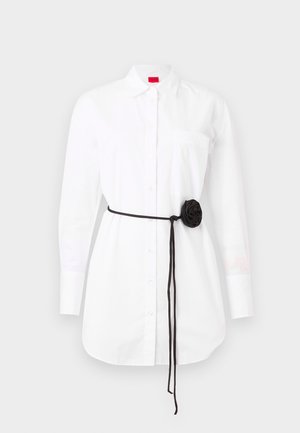 White button-up shirt with long sleeves, chest pocket, and a black fabric belt featuring a rosette detail. Cotton material with a smooth texture.