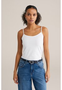 Fehér pamut ujjatlan felső, pántos kivitelben, magas derekú kék farmernadrággal párosítva. Fekete öv ezüst csattal.