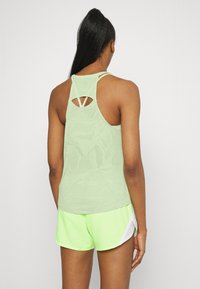 Světle zelený sportovní top s texturovaným vzorem a výstřihem na zádech, doplněný o jasně neonově zelené šortky se bílými akcenty.