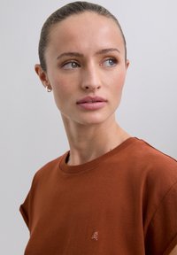 Bruine katoenen t-shirt met korte mouwen, ronde halslijn en een geborduurd schedellogo op de borst. Gladde textuur, casual ontwerp.