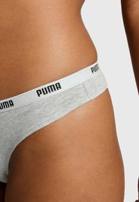 Graue String-Unterwäsche mit einem weißen, mit "PUMA" gebrandeten elastischen Bund. Das Material scheint weich mit einer glatten Textur zu sein.