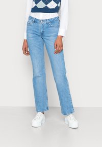 Jean droit bleu clair en denim, avec des poches avant et des détails de couture subtils, associés à des baskets blanches.