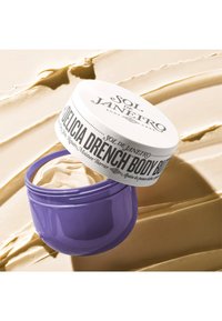 Lilla krukke med kroppskrem, med hvitt lokk med svart tekst. Kremet, off-white produkt synlig inni, med en teksturert bakgrunn.