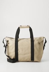 Beige waterproof duffel bag with black webbed straps, a detachable shoulder strap, and a snap-button handle. Features embossed logo.