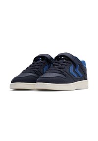 Mörkblå sneakers tillverkade av mocka och nätmaterial, med en kardborreband, snörning och en lättfärgad gummisula. Tre blå ränder på sidan.