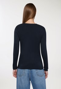 Granatowy sweter z długimi rękawami, okrągłym dekoltem, ściągaczami przy mankietach i hemie, wykonany z miękkiego materiału. Noszony z jasnoniebieskimi dżinsami.