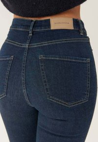 Mörkblå jeans i denim, med en åtsittande design, två bakfickor och en tan-färgad etikett med "BUBBLEROOM" vid midjan.