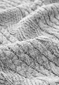 Szara dzianina o fakturowanym, wzorowanym designie z podniesionymi warkoczami i subtelnymi odcieniami szarości. Miły i przytulny wygląd.