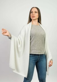 Châle blanc drapé en tissu doux, porté par-dessus un haut gris et un jean. Le châle présente une texture lisse et une silhouette fluide.