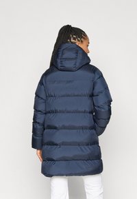 Geacă puffer bleumarin cu glugă, având un design matlasat și mansete ribbed, lungime până la genunchi cu un exterior neted și strălucitor.