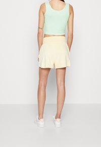 Crop top a coste verde chiaro abbinato a pantaloni corti in mussola gialla. Sneakers bianche con un accento rosa pastello sul tallone.