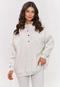 Jasnoszary sweatshirt o luźnym kroju, okrągłym dekolcie, zapięciem na cztery guziki i ściągaczami przy rękawach. Miękka faktura, minimalistyczny design, brak wzorów.