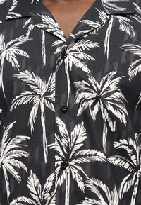 Μαύρο πουκάμισο με κουμπιά και λευκά σχέδια φοίνικων, με γιακά, φορεμένο από άτομο με μεσαία σκούρο τόνο δέρματος.