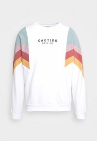 Hvid sweatshirt med multicolore chevron-striber i teal, pink, rød og gul på ærmerne. Har "KAOTIKO" logoet på brystet.