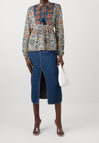 Blusa a fantasia con maniche lunghe, dotata di una scollatura con fiocco. Abbinata a una gonna a tubino in denim scuro con spacco frontale. Sandali con tacco trasparente.